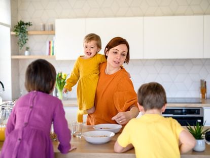 Woman with son and daughters preparing breakfast, using smartphone.