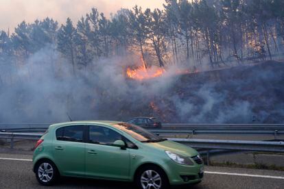 Un coche circula por la A-8 en Luarca, ante las llamas del incendio registrado en la región asturiana, el viernes.