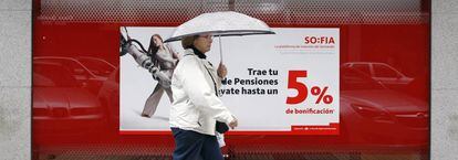 Una mujer camina frente a una sucursal bancaria en la que se anuncian planes de pensiones.