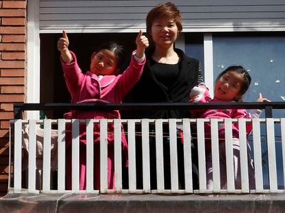 Wei Chen y sus hijas saludan desde el balcón de su piso de Barcelona, donde llevan una semana confinadas.
