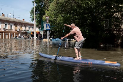 Un hombre utiliza una tabla de paddle surf para moverse por una calle inundada en Jersón. 