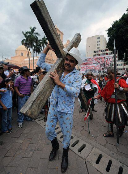 Un partidario de Zelaya, en pijama y con el sombrero típico del presidente depuesto, carga una cruz durante un acto cultural, este domingo en Tegucigalpa.