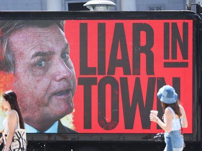 Varias personas pasan frente a un cartel que tilda a Bolsonaro de mentiroso en Los Ángeles (EE UU), durante la Cumbre de las Américas.
