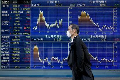 Un hombre camina frente a un tablero electrónico con los índices de la Bolsa de Tokio.