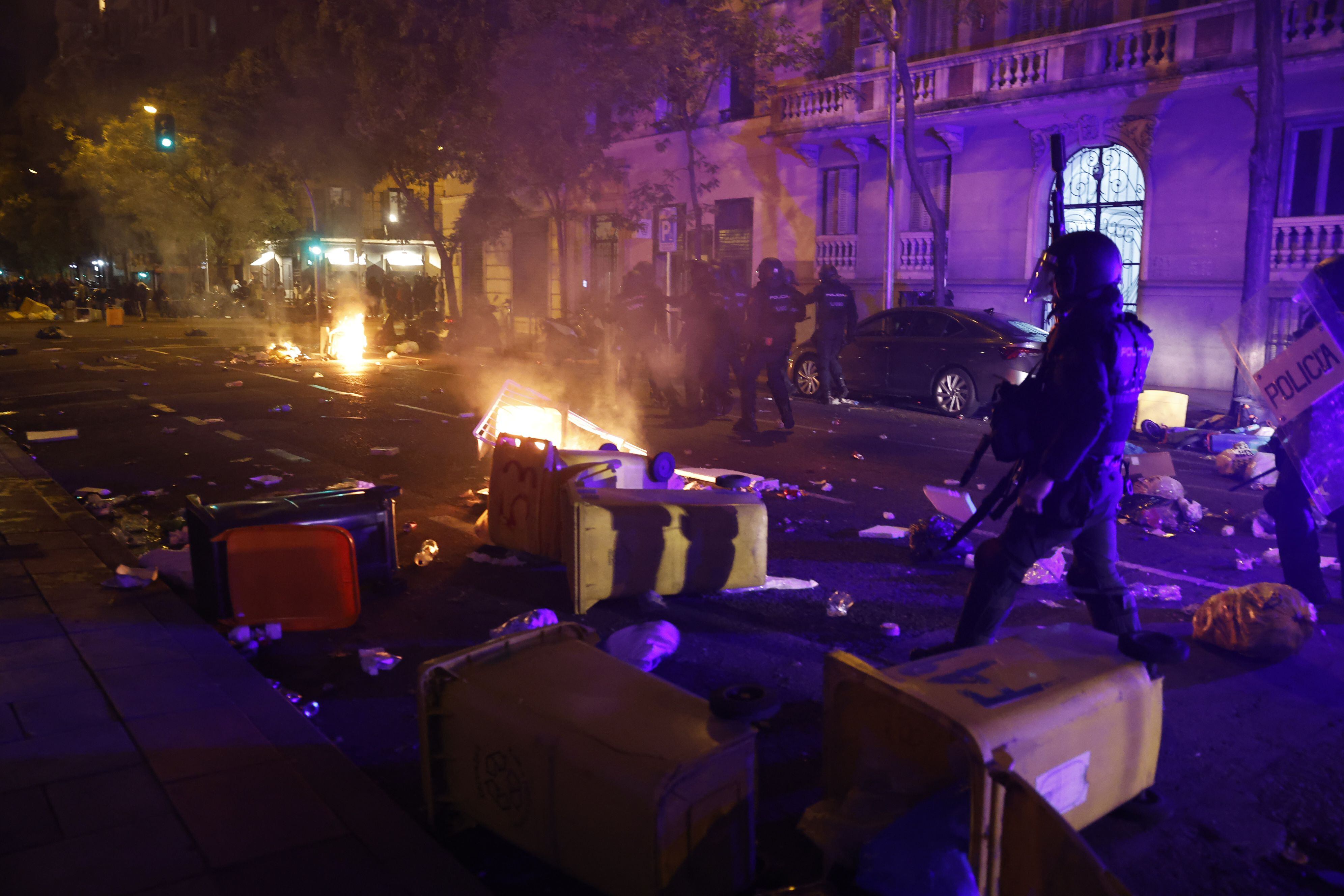 Agentes de policía se abren paso entre los contenedores quemados por los ultras tras la manifestación. 