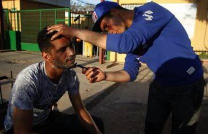 Un refigiado sirio afeita a un compañero en las puertas del CETI de Melilla