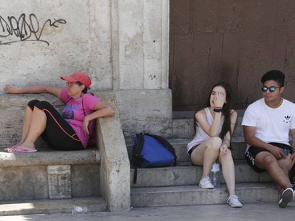 Tres personas a la sombra en la plaza de la Virgen de Valencia.