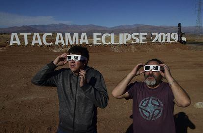 Dos turistas miran al sol antes del eclipse solar con unas gafas especiales, en el desierto de Atacama.