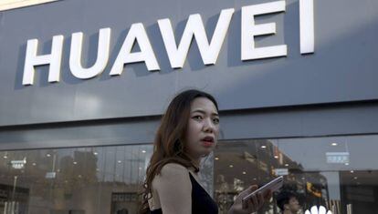 Una mujer usa un teléfono móvil junto a un establecimiento de Huawei en Pekín