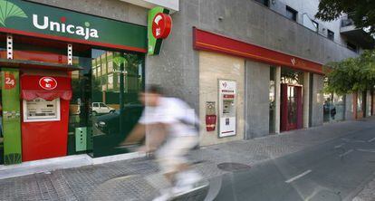 Un ciclista cruza frente a oficinas de Unicaja y Cajasur, en Sevilla.