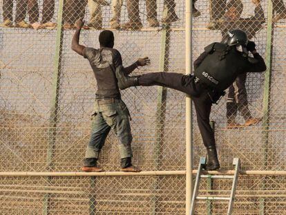 Un agente trata de alcanzar a un inmigrante encaramado en la valla de Melilla.