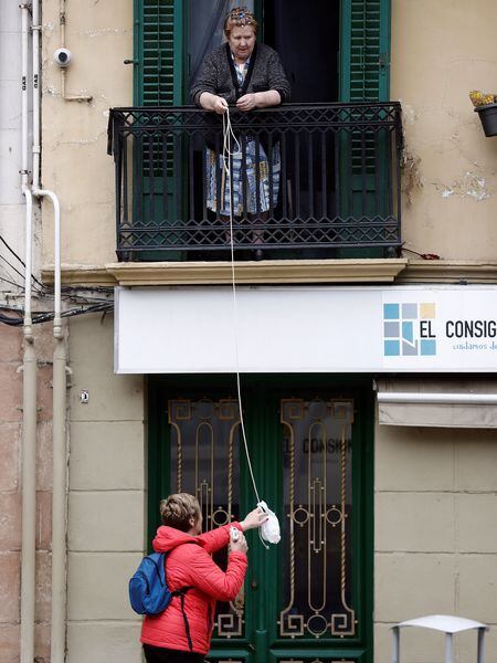 Una mujer facilita comida a una persona mayor gracias a una bolsa colgada de una cuerda desde su balcón.