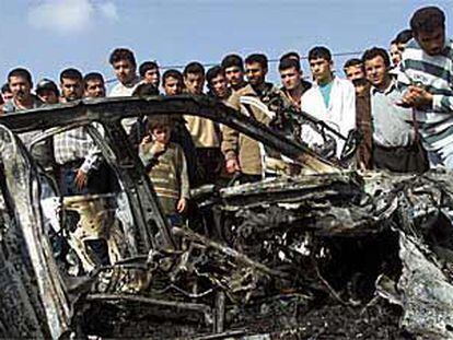 Refugiados de Gaza, junto a los restos del coche en el que  un guardaespaldas de Arafat fue abatido por el Ejército israelí en febrero.