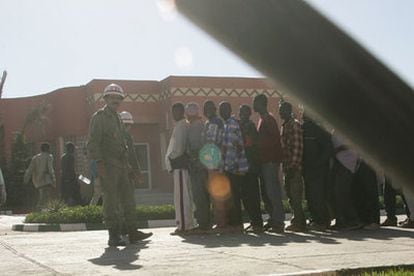 Varios inmigrantes subsaharianos forman fila, vigilados por un policía militar, en un cuartel de Guleimin.
