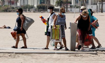 Varias personas protegidas con mascarillas acceden a la playa de la Malvarrosa de Valencia.