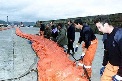 Personal de Protección Civil prepara las barreras de contención del fuel en el puerto de Fisterra.