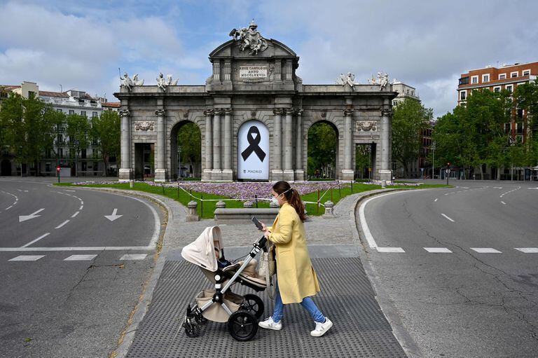 Una mujee con un carrito de bebé pasa ante la Puerta de Alcalá de Madrid, con un lazo negro en señal de duelo.