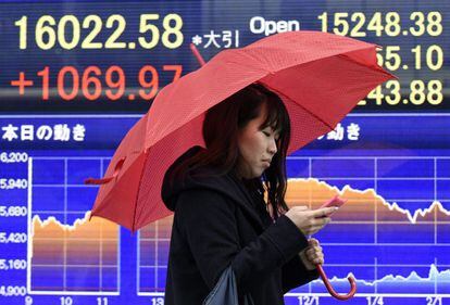 Una mujer camina junto a una pantalla con información bursátil en Tokio