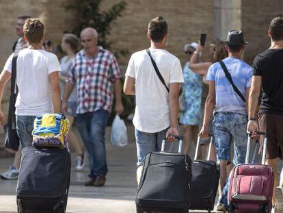 Cuatro j&oacute;venes turistas caminan con su maletas en Valencia. 
