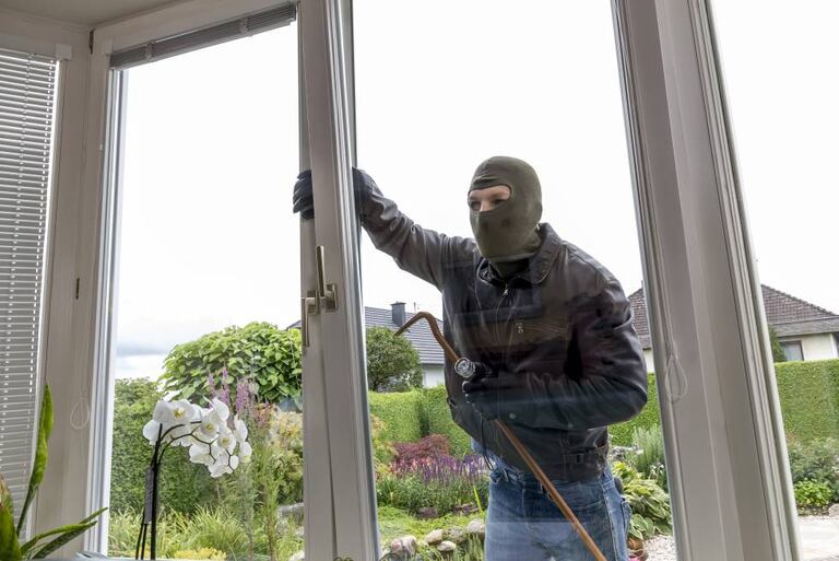 Un ladrón intenta entrar por la ventana de una casa, forzándola.