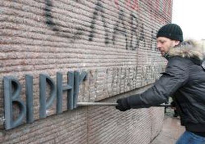 Un manifestante retira una placa de un monumento de la era sovi&eacute;tica.