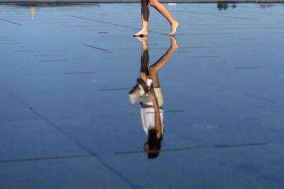 Una mujer camina sobre el suelo de espejo de una fuente de Burdeos, Francia.