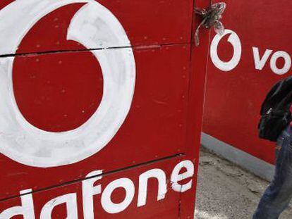Un hombre habla con su m&oacute;vil al lado de un logotipo de Vodafone.