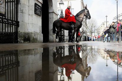 Un guardia a caballo se refleja en un charco mientras los turistas lo fotografían, en Londres (Gran Bretaña).