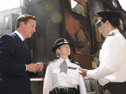 El primer ministro británico, David Cameron, y dos policías, frente a un edificio incendiado durante los disturbios