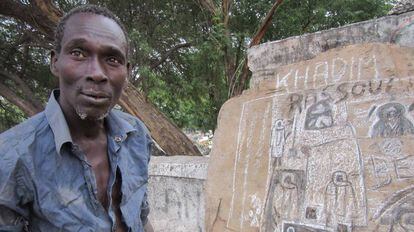 Pape Diop, junto a algunos de sus dibujos en el muro del cementerio de la Medina, en Dakar.