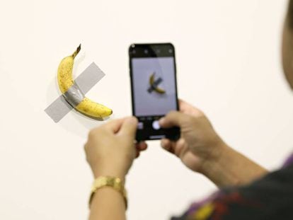Un visitante saca una foto del plátano adherido a la pared, del artista Maurizio Cattelan.