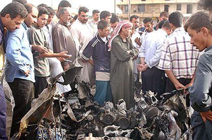 Decenas de iraquíes observan los restos del coche bomba utilizado en el atentado de ayer en Faluya.