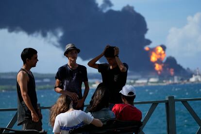 El fuego se desató el viernes por la tarde después de que a las 19 horas un rayo impactara en uno de los tanques de la base de supertanqueros. A las 5.00 horas del sábado, el fuego se extendió a un segundo depósito, acrecentando la catástrofe. En la imagen, un grupo de jóvenes se reúne en un muelle mientras las llamas y el humo continúan saliendo de la base de supertanqueros de Matanzas.