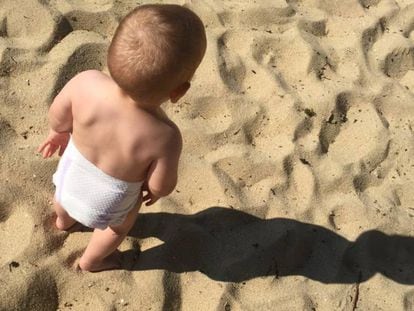 Un bebé en pañales juega en la playa.