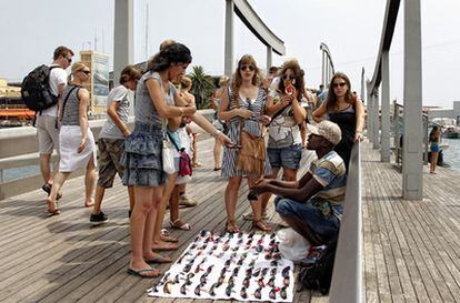 Fotografía de archivo en la que un 'mantero', inmigrante subsahariano, vende gafas de sol a los turistas que cruzan la Rambla de Mar hacia el Maremagnum en el puerto de Barcelona.