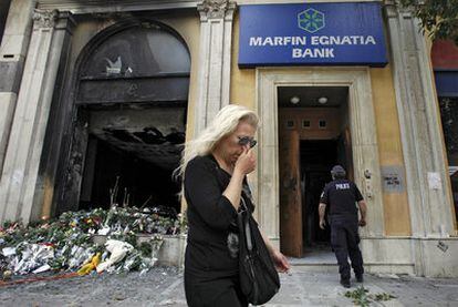 Una mujer pasa ayer por delante de la oficina bancaria incendiada en Atenas.