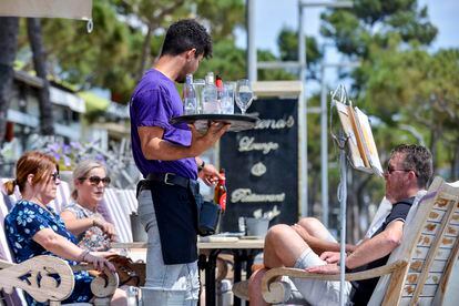 Un camarero atiende a unos clientes de una mesa, en la terraza de un restaurante del paseo marítimo de Platja d'Aro (Girona).