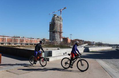 Dos ciclistas pedalean por Madrid Río ante la nueva torre de Legazpi.
