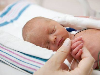 Una madre sostiene la mano de un bebé en una incubadora.