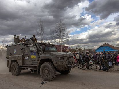 Unos soldados ucranios saludan desde un vehículo militar a los residentes que esperan en una cola para recibir ayuda humanitaria, en la ciudad de Trostyanets, Ucrania, el 29 de marzo de 2022.