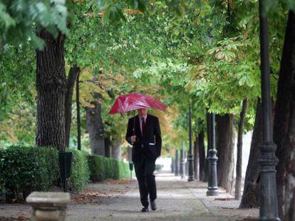 Un hombre pasea por el Retiro bajo un paraguas.
