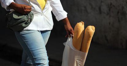 Una mujer camina con dos barras de pan en una bolsa de pl&aacute;stico.