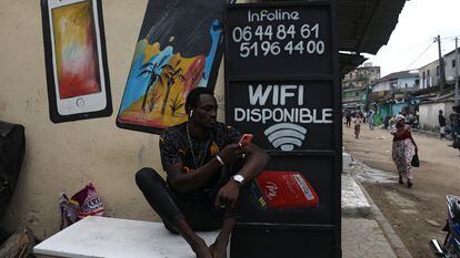 Un ciudadano navega por internet desde su móvil junto a un locutorio en una calle de Abiyán, Costa de Marfil.