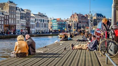 Decenas de turistas descansas a orillas de uno de los canales de Ámsterdam.