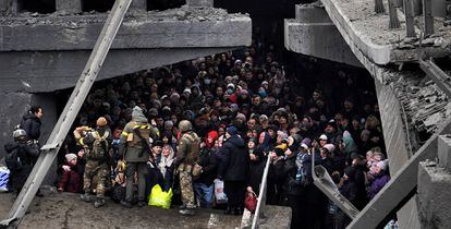 Ucranios intentan pasar por debajo de un puente destruido en Irpín, cerca de Kiev, este sábado.