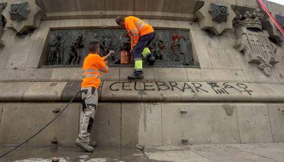 Dos operaris netegen les pintades al monument a Colom.
