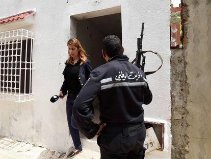 Un agente tunecino junto a una periodista que abandona la casa en la que dos yihadistas han muerto este mi&eacute;rcoles. 