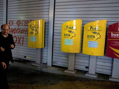 Dos hombres caminan frente a la oficina postal de Atenas, este lunes.