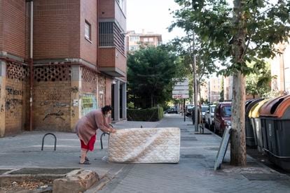 Una mujer arrastra un colchón hasta unos contenedores de basura en el barrio de Pan Bendito, en Carabanchel (Madrid).