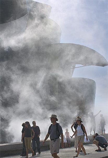 Varias personas se refrescan en el exterior del Museo Guggenheim durante la emisión de vapor de agua.